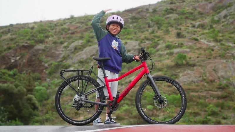 Child standing beside a red woom bicycle
